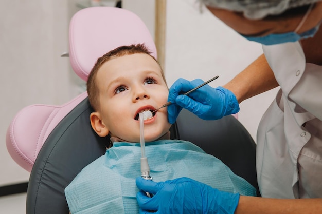 El dentista pediátrico trata la caries infantil y la cavidad bucal del niño sentado en la silla del dentista durante el chequeo médico regular