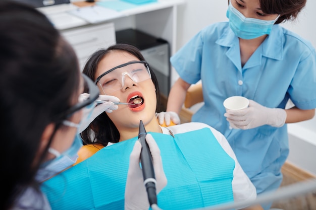 Dentista perforando los dientes del paciente joven que sufre de dolor de muelas