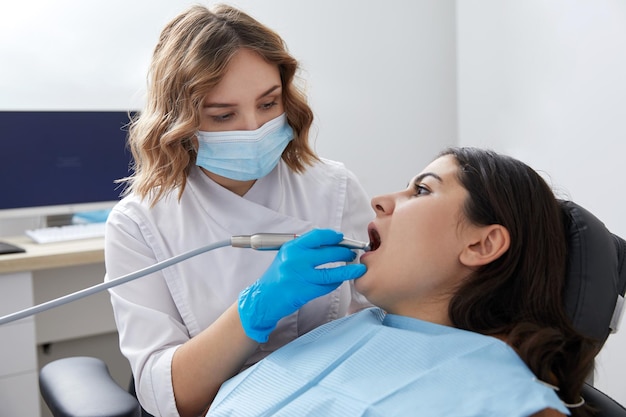 Dentista perfurando o dente de uma paciente em cadeira dentária