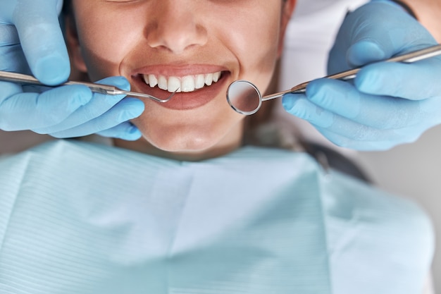 Foto dentista positivo alegre y cliente en odontología. paciente de sexo femenino en el procedimiento dental, médico con instrumentos dentales en la clínica dental moderna, de cerca.