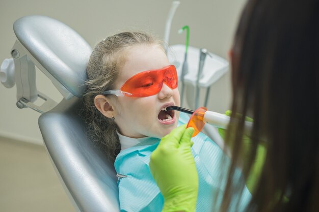 Dentista preparando luz ultravioleta antes de hacer empastes dentales para paciente niña pequeña