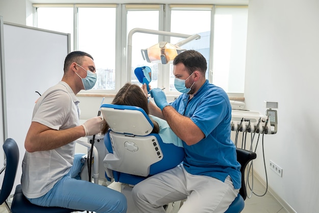 Dentista profesional con asistente trata dientes paciente mujer joven acostado en una silla dental en una clínica dental