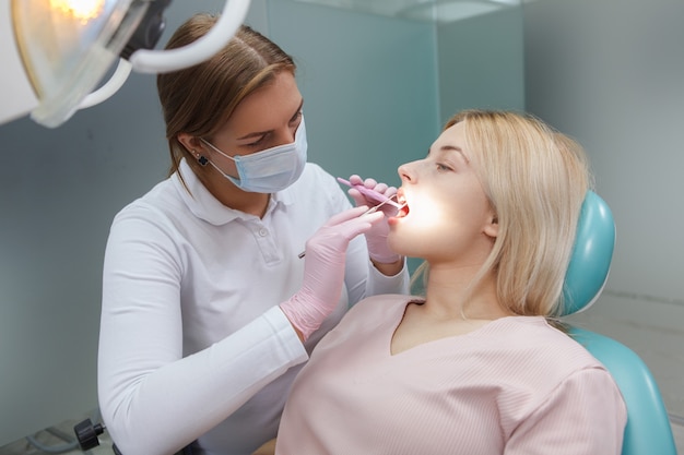 Dentista profesional con mascarilla médica, examinando los dientes de la paciente