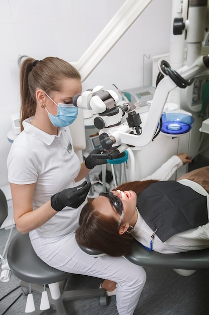Dentista profesional con mascarilla médica, con microscopio dental en el paciente