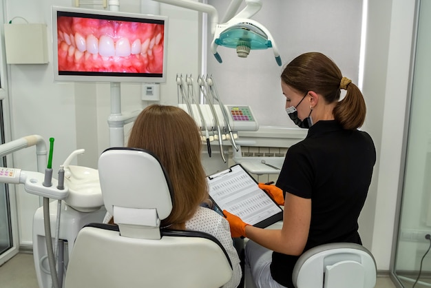 Dentista profesional con portapapeles hablando o grabando el diagnóstico con el paciente antes o después del tratamiento