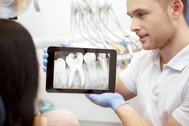 Dentista profesional que muestra a su cliente radiografías en una tableta digital