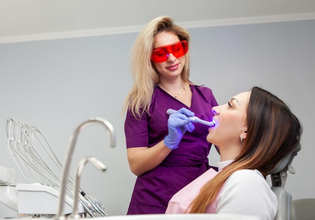 Dentista profissional faz procedimentos de branqueamento dos dentes para o paciente na clínica dentária