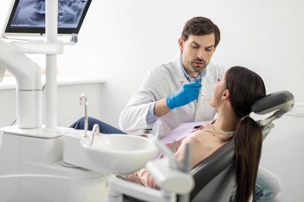 Dentista profissional masculino examinando dentes de jovens pacientes femininas em consultório de odontologia moderno grátis