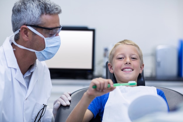 Dentista que ayuda al paciente joven mientras se cepilla los dientes