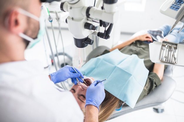 Dentista que controla los dientes del paciente femenino con las herramientas dentales