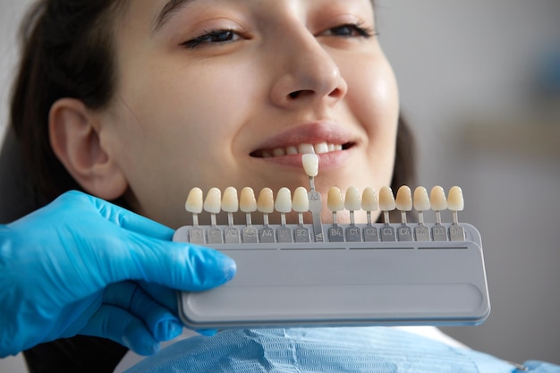 Dentista que elige el color del esmalte dental para el dentista paciente que aplica la muestra de la escala del esmalte dental
