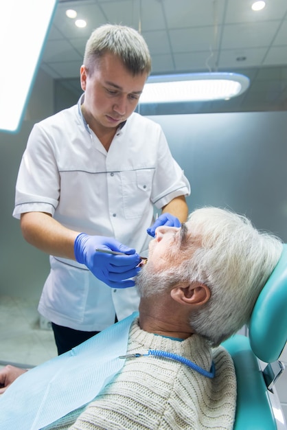 Dentista que examina al paciente anciano en la práctica médica y calificación de la silla dental