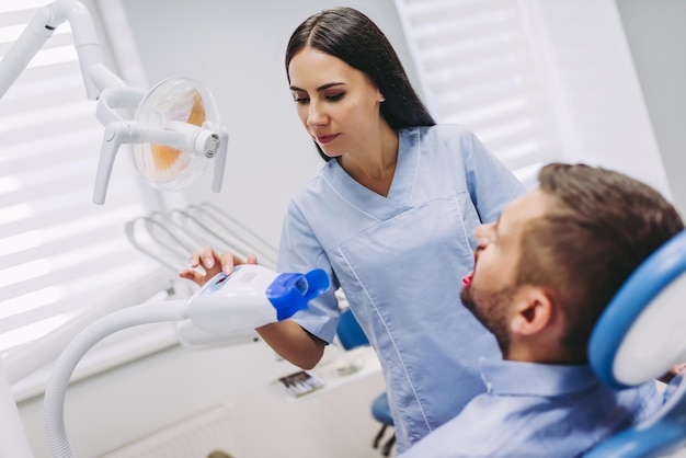 Foto dentista que prepara la lámpara ultravioleta para el procedimiento dental con los dientes del paciente en la clínica dental moderna