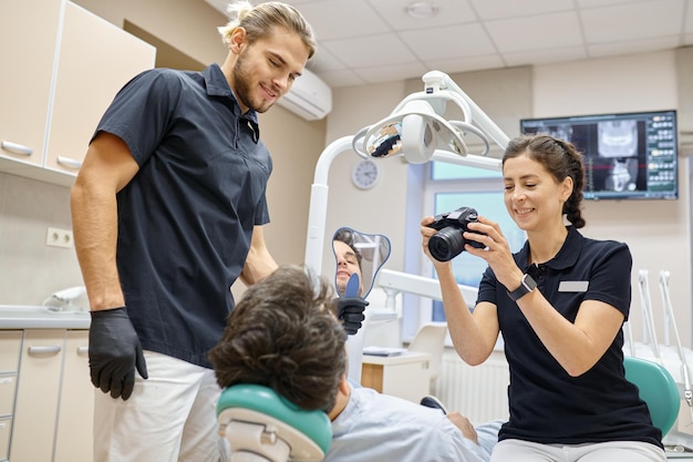 Dentista que usa una cámara digital para hacer una foto de los dientes del paciente después del tratamiento. servicio de clinica dental