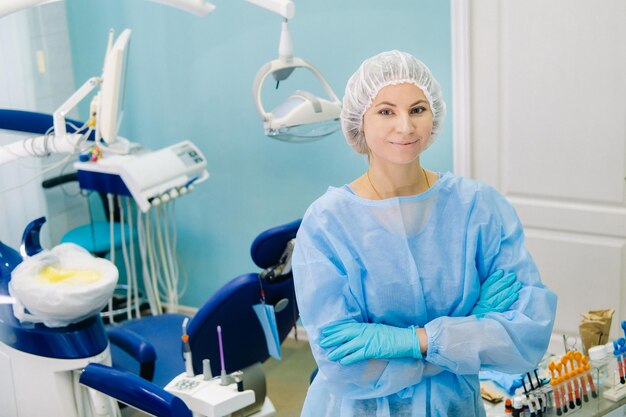 Una dentista que usa una máscara médica y guantes de goma posa para la cámara y cruza los brazos en su oficina