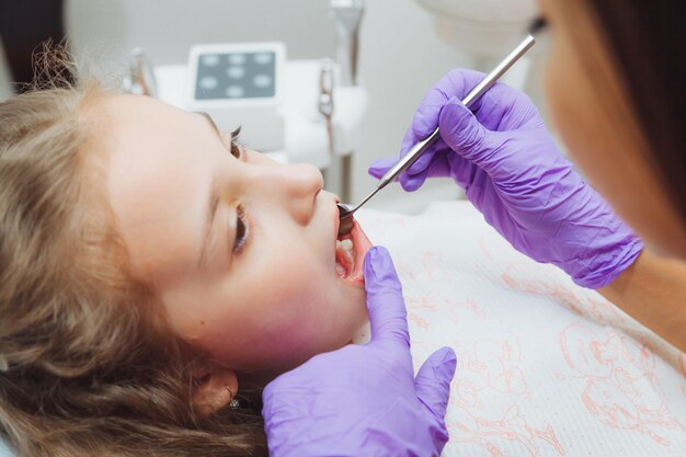 El dentista realiza un procedimiento de examen en una niña linda Niña sentada en el consultorio del dentista