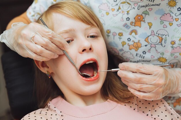 El dentista realiza un procedimiento de examen en una niña linda Niña sentada en el consultorio del dentista