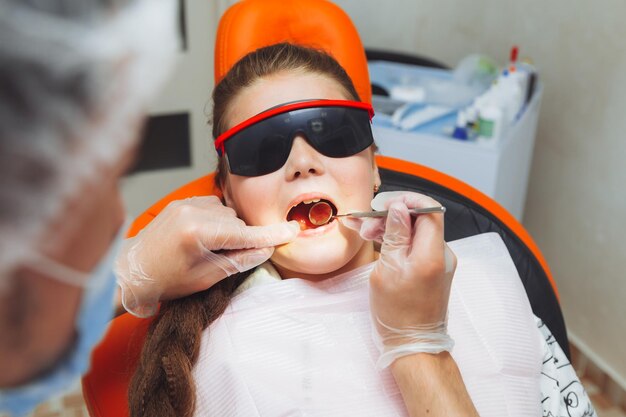 El dentista realiza un procedimiento de examen en una niña linda Niña sentada en el consultorio del dentista