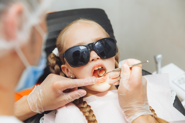 El dentista realiza un procedimiento de examen en una niña linda Niña sentada en el consultorio del dentista