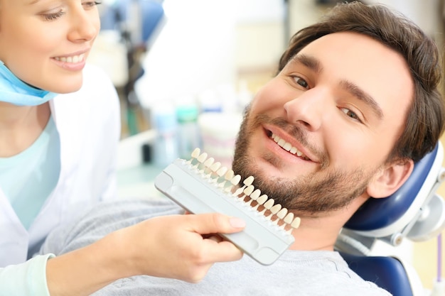 Dentista revisando y seleccionando el color del primer plano de los dientes del joven