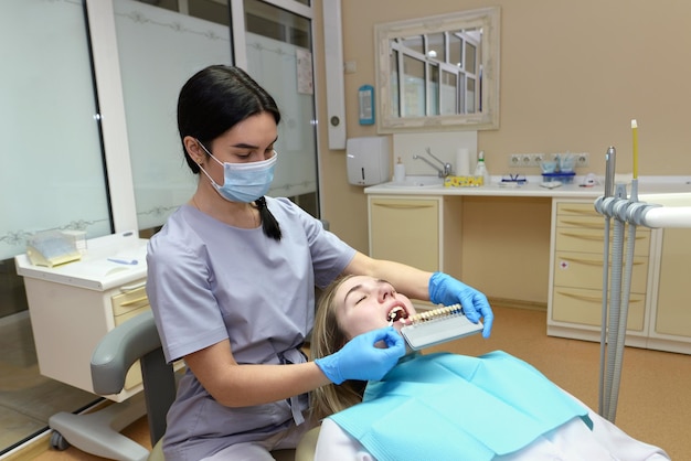 Dentista revisando y seleccionando el color de la selección de color de dientes de mujer joven