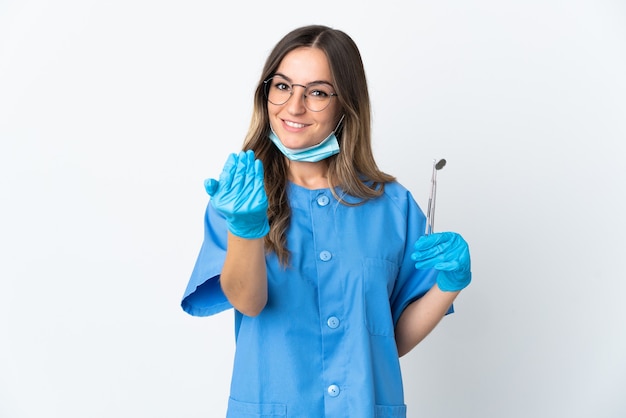 Dentista rumano mujer sosteniendo herramientas sobre aislado en pared rosa invitando a venir con la mano. Feliz de que hayas venido