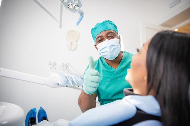 Un dentista satisfecho durante una visita con un paciente levanta los pulgares