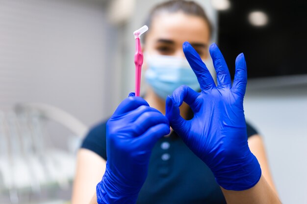 Dentista segura escova para limpeza dos espaços interdentais e faz gesto de ok