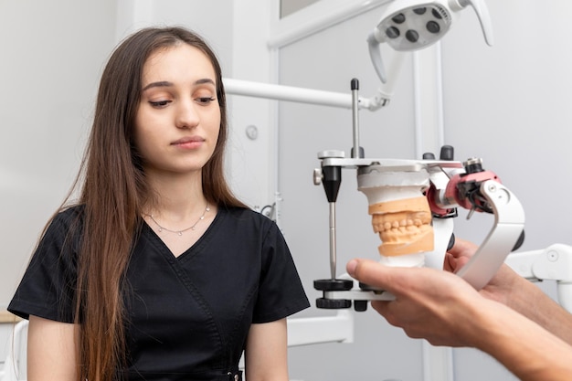 Dentista segurando articulador dentário com modelo de prótese de gesso dental mostrando a um paciente