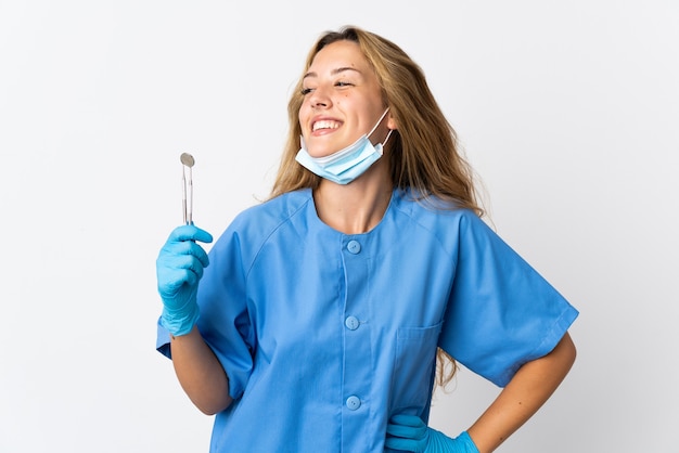 Foto dentista segurando ferramentas isoladas no fundo branco, posando com os braços na cintura e sorrindo