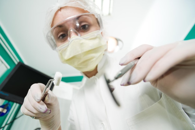 Dentista segurando pinças dentárias com almofada de algodão e espelho angulado para inspecionar um paciente. Foco Seletivo.
