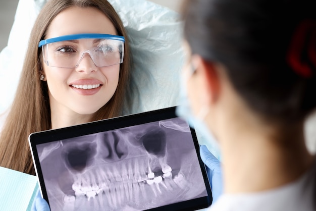 Dentista segurando um tablet digital com uma imagem de dentes nas mãos na frente de uma paciente