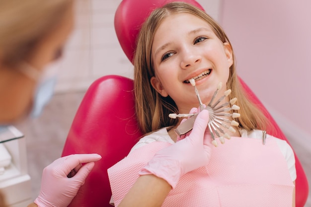 El dentista selecciona el color de la corona dental de una adolescente en una clínica dental