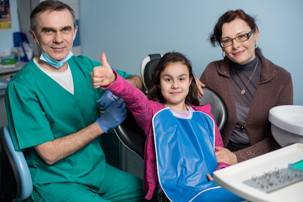 Dentista sênior e menina com a mãe na visita odontológica no consultório odontológico