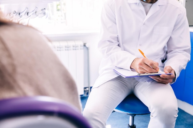 Dentista sentado na cadeira e registra as respostas do paciente de