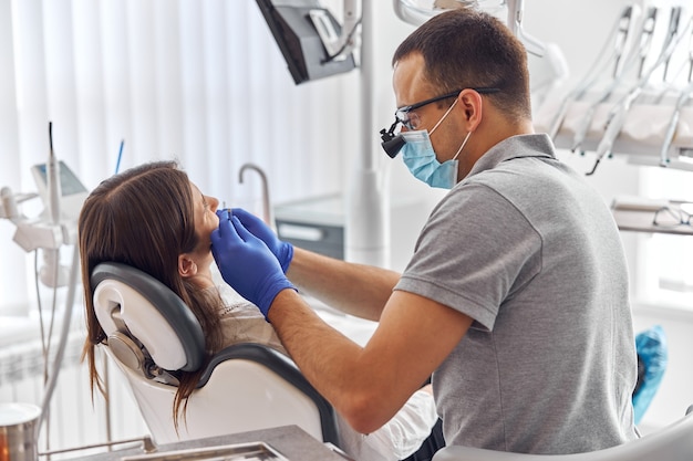 Dentista serio en mascarilla y cliente de pie y comprobando el estado de los dientes. Concepto de salud y medicina.