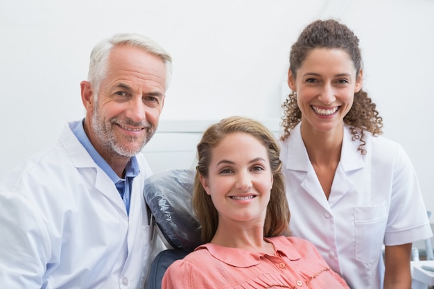 Dentista, seu assistente e paciente sorrindo para a câmera