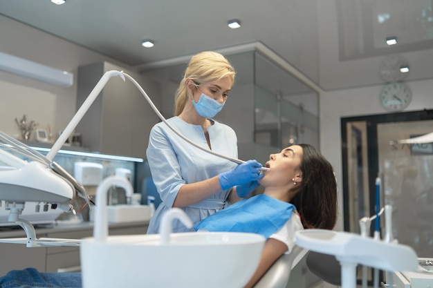 Dentista de sexo femenino en la clínica dental que proporciona examen y tratamiento de la cavidad oral para el paciente femenino