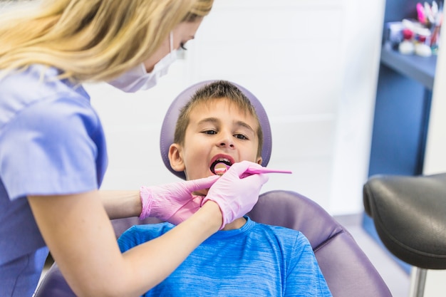 Dentista de sexo femenino que comprueba los dientes del paciente del niño con el espejo dental