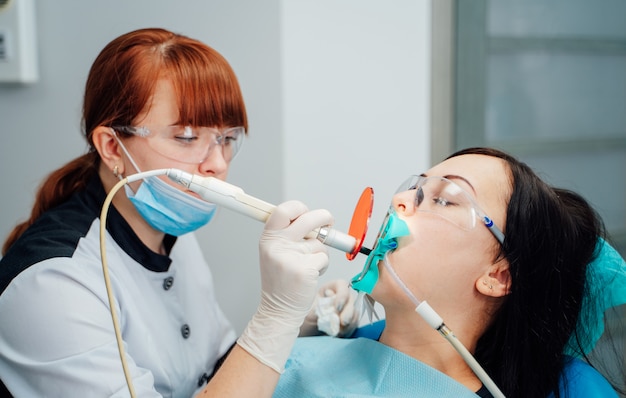 Dentista de sexo femenino que trata los dientes pacientes de la mujer. Médico de estomatología tratando dientes de mujer en clínica de odontología
