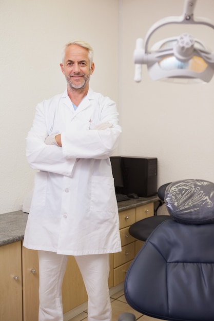 Foto dentista sorrindo para a câmera ao lado da cadeira