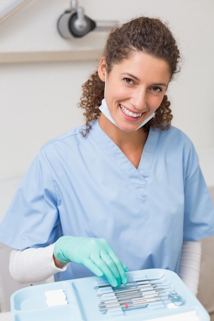Dentista sorrindo para a câmera enquanto escolhe ferramentas