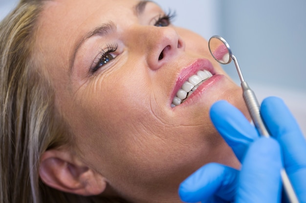 Dentista sosteniendo espejo en ángulo por mujer en clínica médica