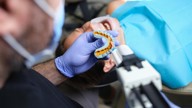 Dentista sostiene yeso con carillas en modelo de yeso y paciente en clínica dental
