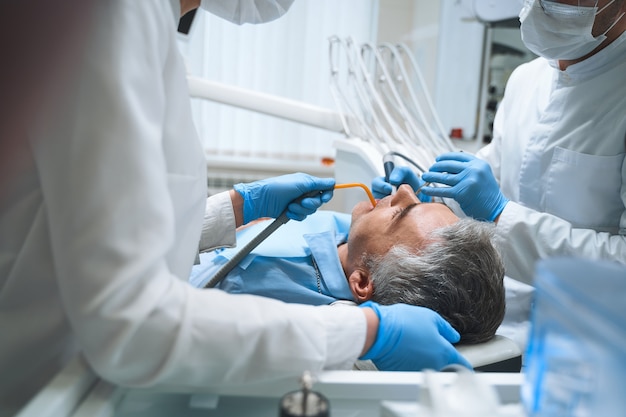 El dentista y su asistente están tratando al hombre en el sillón dental y le están dando tratamiento de conducto.