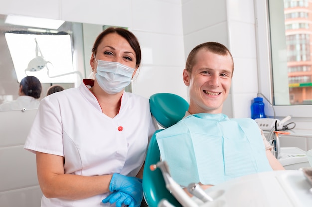 La dentista y su paciente feliz miran a la cámara y sonríen. Recepción en el dentista, dientes sanos, paciente feliz, dientes bonitos.