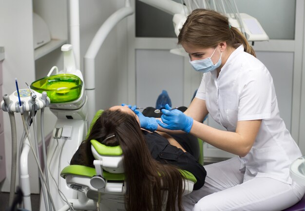 Dentista en el trabajo examinando los dientes de la mujer en la clínica dental