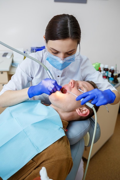 Una dentista trata la caries en los dientes de un paciente masculino en una clínica dental durante la pandemia de coronavirus. Enfoque selectivo