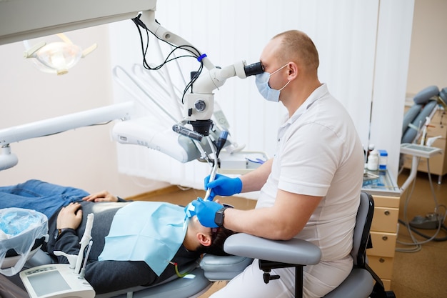 El dentista trata los dientes de su paciente con un microscopio. El dentista trata la boca del paciente. Cuidado dental. Foto de alta calidad