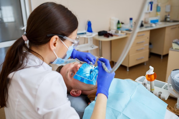 Un dentista trata a un paciente masculino con instrumentos dentales. El dentista examina los dientes de los pacientes en la clínica dental. Enfoque selectivo